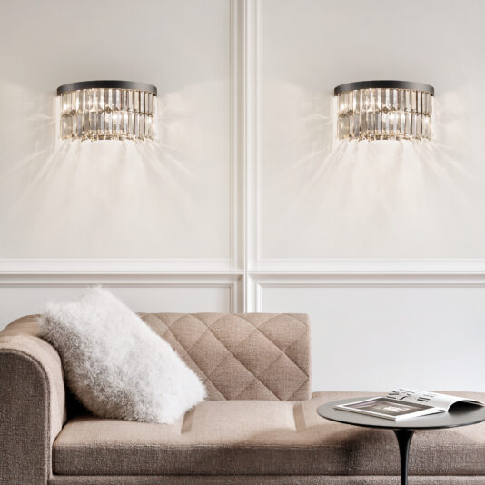 Modern Smoked Cut Crystal Wall Light A beige, tufted sofa with a white pillow sits against a white, paneled wall. Two Modern Smoked Cut Crystal Tiered Chandeliers hang above, casting a soft glow. A round table with a book and magazine stands nearby.