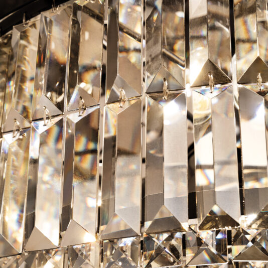 Modern Smoked Cut Crystal Wall Light A close-up of the Modern Smoked Cut Crystal Tiered Chandelier shows rows of rectangular, faceted prisms. The crystals reflect and refract light to create a sparkling display, highlighting the intricate craftsmanship of its design.