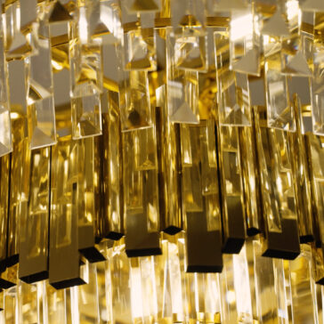 Modern Tiered Crystal Chandelier Detailed view of the Modern Smoked Cut Crystal Chandelier, featuring gold and transparent glass prisms. Light shines through and reflects off them, creating a warm, opulent glow.