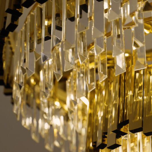 Modern Tiered Crystal Chandelier A close-up of the Modern Smoked Cut Crystal Chandelier reveals rows of vertically hanging smoked cut crystal prisms. Bathed in warm golden light, they shimmer with an alluring effect enhanced by slightly off-center framing.
