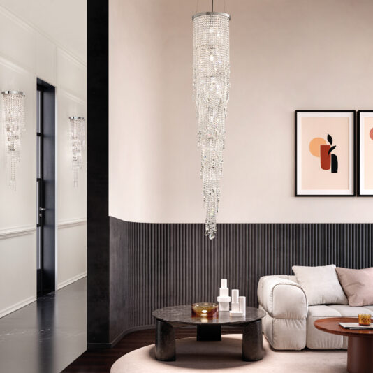 The modern living room showcases a round marble coffee table adorned with décor, a beige sofa, framed abstract art, and is illuminated by a tall crystal chandelier. This complements the Chandelier Style Cut Crystal Wall Light for an elegant mix of light and dark tones.