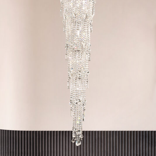 The Chandelier Style Cut Crystal Wall Light features cascading crystals against a light wall, reflecting light for a shimmering effect. The lower portion is accented with vertical, textured black paneling.