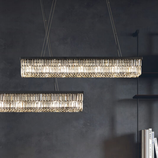 Two Modern Smoked Cut Crystal Chandeliers hang against a dark gray wall, casting a warm glow. A partial shelf with books is visible in the bottom right, adding depth to the chic ambiance.