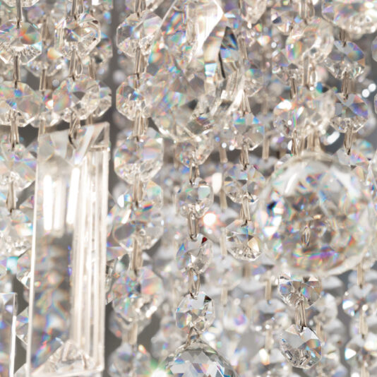 A close-up of the Rectangular Smoked Cut Crystal Ceiling Light (Copy) highlights its sparkling crystals. The light refracts through the varied shapes, producing a rainbow effect with intricate reflections against the blurred background, showcasing brilliant shine and clarity.