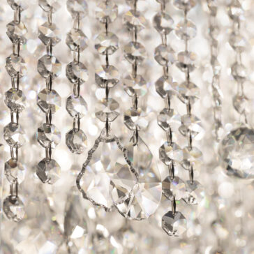 Close-up of sparkling crystal chandelier strands with round and teardrop shapes, reflecting light in various colors. The crystals are intricately arranged, creating a luxurious and elegant appearance.