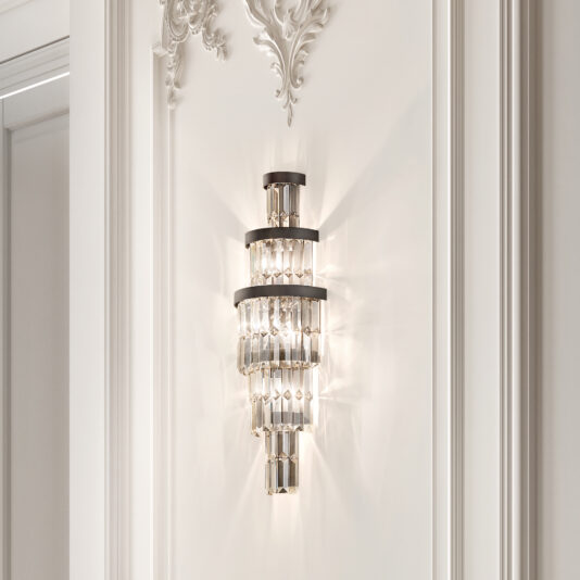 The Smoked Cut Crystal Tiered Wall Light adorns the ornate white wall, its luxurious crystal accents casting a soft, elegant glow that enhances the decorative molding.