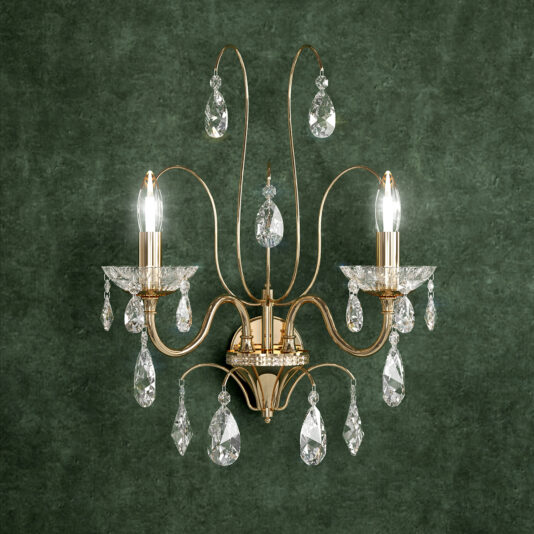 The Classic Cut Crystal Gold Plated Chandelier features two candle-style bulbs and hanging crystal droplets, offering timeless elegance reminiscent of a gold wall sconce, beautifully highlighted against a textured green background.