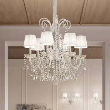 Classic Style Clear Crystal Chandelier The Classic Style Clear Crystal Chandelier boasts elegant arms with hanging crystals and white fabric lampshades. Suspended from a wooden ceiling, it softly illuminates beige walls and room decor.