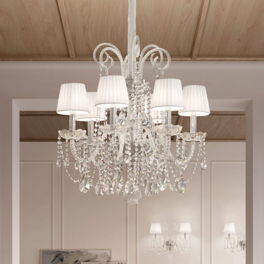 The Classic Style Clear Crystal Chandelier boasts elegant arms with hanging crystals and white fabric lampshades. Suspended from a wooden ceiling, it softly illuminates beige walls and room decor.