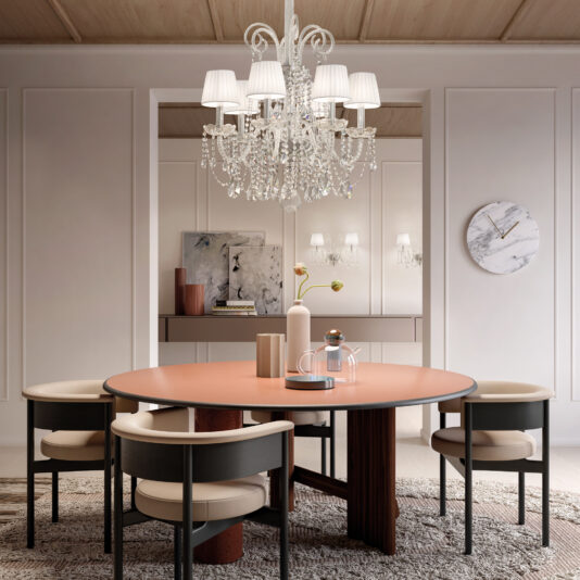 A stylish dining room showcases a round table with four chairs under a Classic Style Clear Crystal Chandelier. The glowing fixture highlights the wooden ceiling, art-adorned walls, and marble clock, while a textured rug covers the floor and a console table with decor completes the scene.