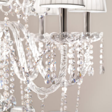A close-up of the Classic Style Clear Crystal Chandelier reveals intricate designs with dangling beads that create a sparkling effect. The shiny surfaces and soft white lampshades atop the light fixtures add an elegant touch to its sophisticated decor.