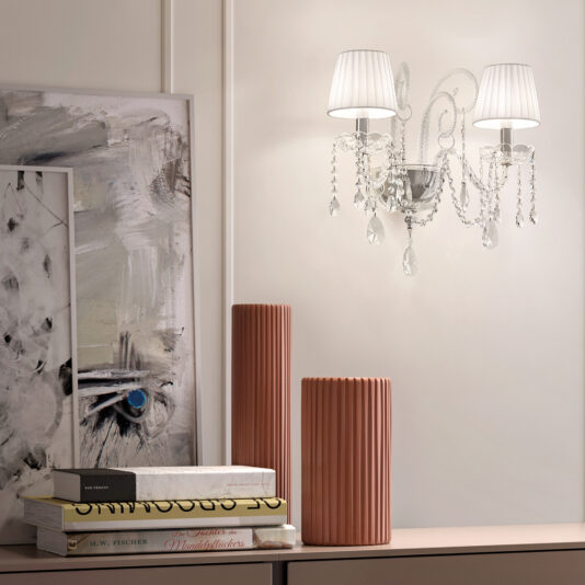 A modern interior features the Classic Style Clear Crystal Wall Light, two ribbed terracotta vases, stacked books, and an abstract painting with a bold blue eye on a neutral wall.