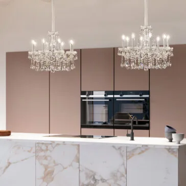 Classic Style Crystal Chandelier A modern kitchen with a marble island, built-in appliances, matte pink cabinets, and two Classic Style Crystal Chandeliers above the island. A black faucet and bowls complete the elegant countertop design.
