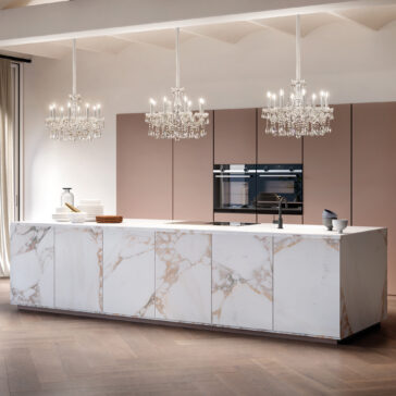 Classic Style Crystal Chandelier A modern kitchen with a large marble island, muted-tone minimalist cabinets, built-in stainless steel appliances, wood flooring, and two Classic Style Crystal Chandeliers overhead.