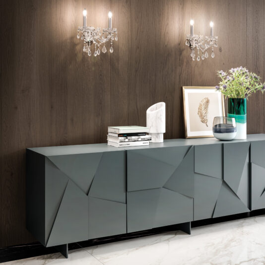 A modern sideboard with angular geometric doors sits against a dark wood wall. Two crystal wall sconces and the Oval Crystal Ceiling Light (Copy) provide elegant lighting, while decor, books, art, and flowers adorn the sideboard.