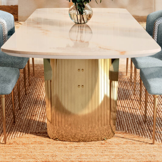 The Large Modern Marble Dining Set features a sleek table with a marble top and gold-finished base, complemented by blue upholstered chairs. A small vase with plants adds elegance to the tabletop, while a textured beige rug completes the look beneath.