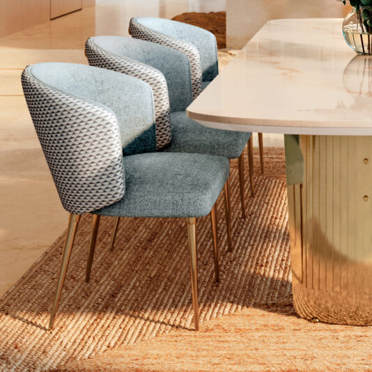 A sleek, modern dining room showcases the Large Modern Marble Dining Set, featuring a table with a polished surface and gold base. Three upholstered chairs in blue and white geometric patterns surround it, all set on a textured beige rug.