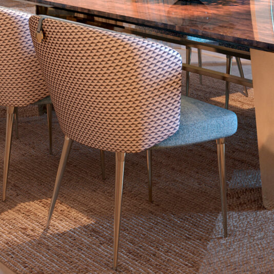 A dining space features the Large Modern Veneered Dining Set, including two contemporary blue and beige patterned chairs with gold legs beneath a wooden table with a reflective surface, all placed on a woven textured natural-toned rug.
