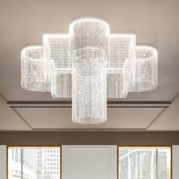 The Modern Oval Smoked Cut Crystal Chandelier features cascading smoked cut crystals in an oval, tiered design hanging from the ceiling, emitting a soft glow, perfectly complemented by tall windows showcasing city building views.