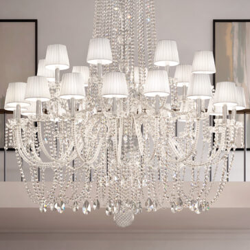 The Tiered Classic Style Clear Crystal Chandelier features multiple arms with white lampshades, sparkling crystal beads, and pendants, adding elegance to any modern, well-lit room.