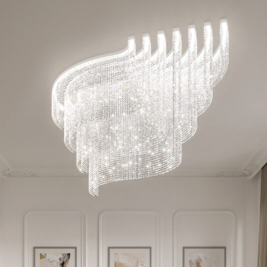The Large Oval Cut Crystal Ceiling Light, featuring an elegant modern wavy design, hangs from a white ceiling. Its chandelier glimmers, with the room’s white walls showcasing molding and framed art.