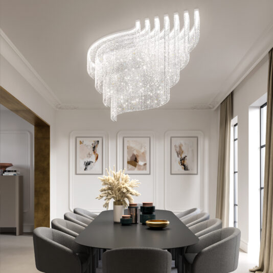 A modern dining room showcases a large rectangular black table with gray chairs around it. The Large Oval Cut Crystal Ceiling Light hangs above. Abstract art decorates the walls, tall windows are dressed with beige curtains, and a vase of pampas grass adorns the table.