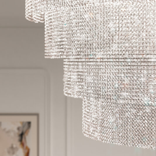 Close-up of a Large Oval Cut Crystal Ceiling Light with cascading layers, glistening softly. A framed artwork on a white wall in the background hints at a sophisticated interior setting.