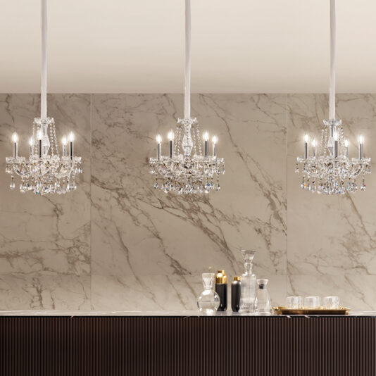 Three crystal chandeliers with lit candles hang above a dark counter set with glassware and candles. An Ornate Crystal Wall Light (Copy) against a light marble backdrop adds modern elegance to the scene.