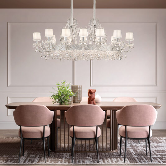 A modern dining room features a wooden table, six blush pink chairs, the Round Silver Leaf Crystal Chandelier (Copy), and decorative accents—plants, vases, sculpture—all set against a neutral paneled wall.