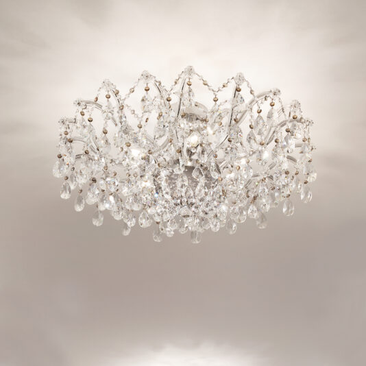 The Round Crystal Ceiling Light features intricate ornate detailing and hanging crystal droplets, mounted on a white ceiling and illuminated with soft, warm light.