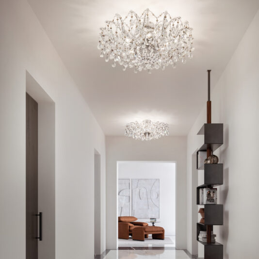 A modern hallway with white walls, two Round Crystal Ceiling Lights, a glossy tile floor, a brown armchair and abstract art in the room at the end, and a contemporary vertical shelving unit on the right.