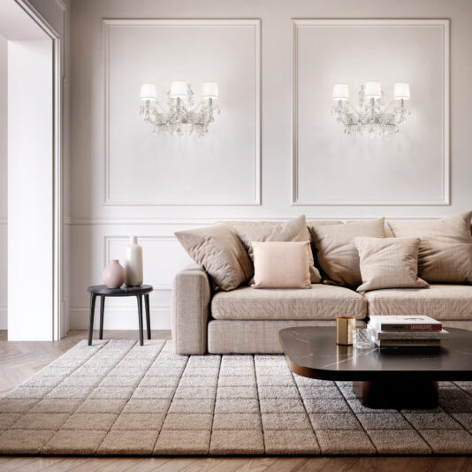 Modern living room with a beige sofa, neutral cushions, textured rug, dark coffee table, side table with vases, and two Classic Style Clear Crystal Wall Light (Copy) fixtures accenting the white paneled wall.