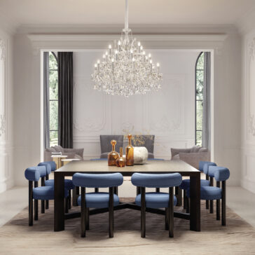 An elegant dining room features a large wooden table with blue cushioned chairs, two sofas in a cozy seating area, and the Contemporary Crystal Drop Chandelier overhead. Light pours in through tall arched windows.