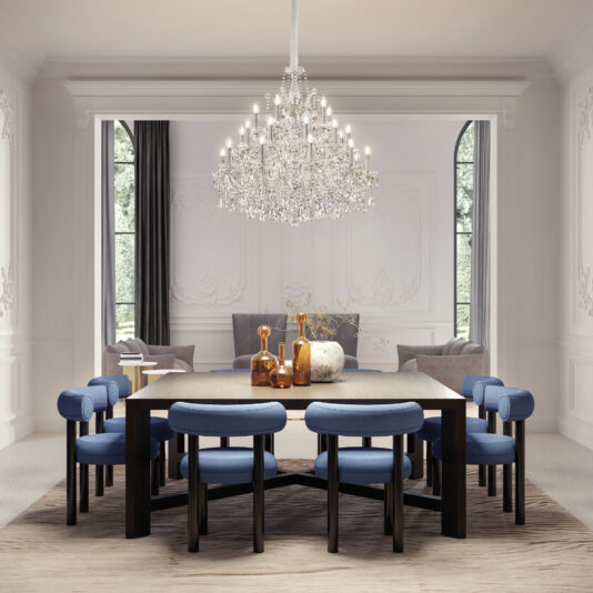 Contemporary Crystal Drop Chandelier An elegant dining room features a large wooden table with blue cushioned chairs, two sofas in a cozy seating area, and the Contemporary Crystal Drop Chandelier overhead. Light pours in through tall arched windows.