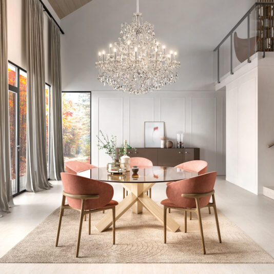 A modern dining room with a round glass table, six pink velvet chairs, neutral walls, and tall curtained windows overlooking autumn trees is illuminated by the Contemporary Tiered Crystal Chandelier.