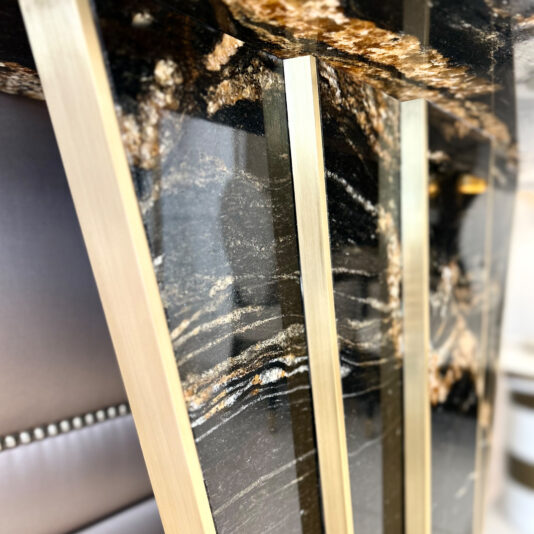 Close-up of the Exclusive Art Deco Style Console Table featuring a glossy black and gold marble top with gold metal legs. A tufted gray chair with metallic studs is partially visible, enhancing the space’s sleek, luxurious style.