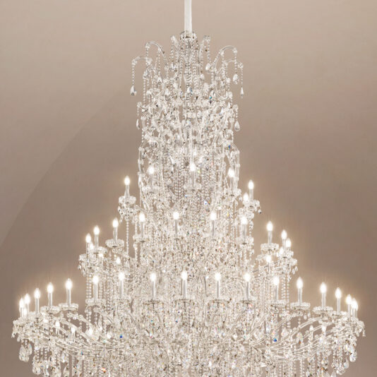 Grand Tiered Crystal Empire Chandelier The Grand Statement Tiered Crystal Chandelier hangs elegantly from the ceiling, showcasing multiple sparkling crystal tiers and numerous bulbs against a neutral backdrop.