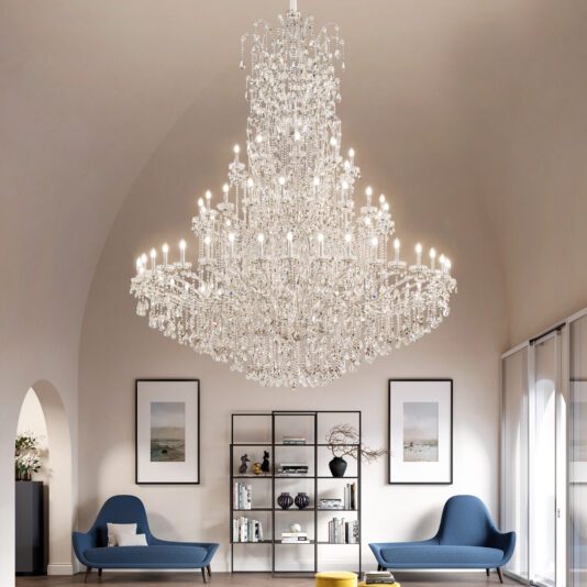 Grand Tiered Crystal Empire Chandelier The Grand Statement Tiered Crystal Chandelier hangs from a vaulted ceiling above two blue modern chairs and a black shelving unit in a stylish, minimalist living room accented with framed art.