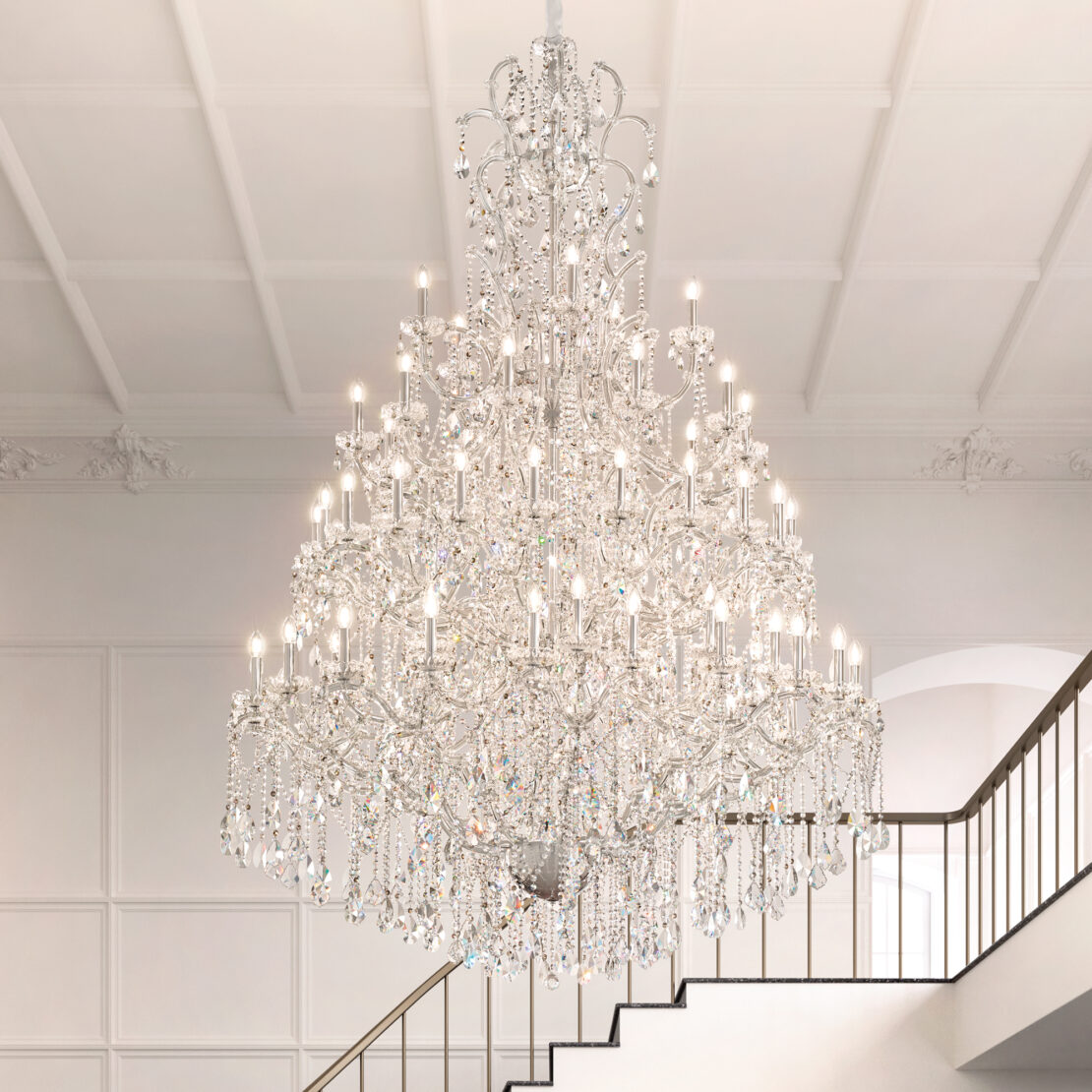 The Grand Crystal Crystal Chandelier (Copy) hangs from a high ceiling in a majestic interior with white walls and a staircase to the right, illuminating the space with its many brilliant lights.