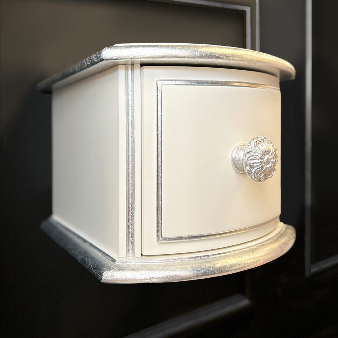The Small Classic Style Floating Bedside in cream and silver features a single ornate knob and decorative trim, beautifully set against a dark background.