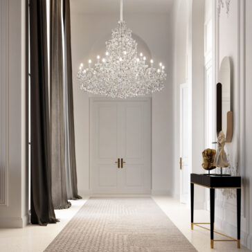 Tiered Clear Crystal Chandelier A grand hallway with white walls and double doors features the Tiered Clear Crystal Chandelier, tall dark curtains, a textured rug, and a console table adorned with sculptures and a mirror.