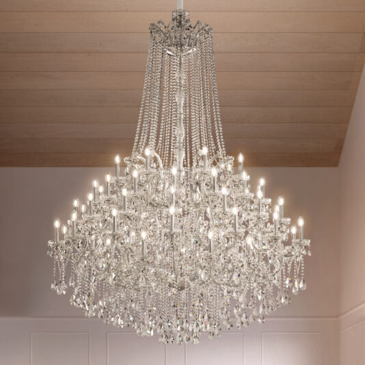 The Grand Tiered Crystal Empire Chandelier (Copy), featuring multiple lit bulbs and cascading crystal strands, hangs from a wood-paneled ceiling in an elegant, softly lit room with pale walls.