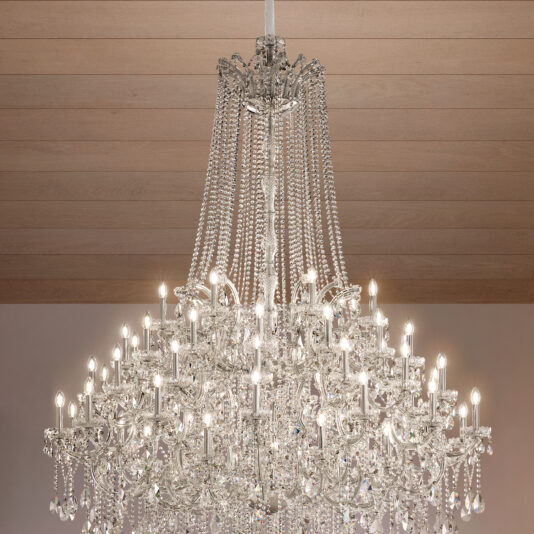 The Grand Tiered Crystal Empire Chandelier (Copy) features multiple lit bulbs and cascading crystal strands, elegantly suspended from a wooden ceiling.