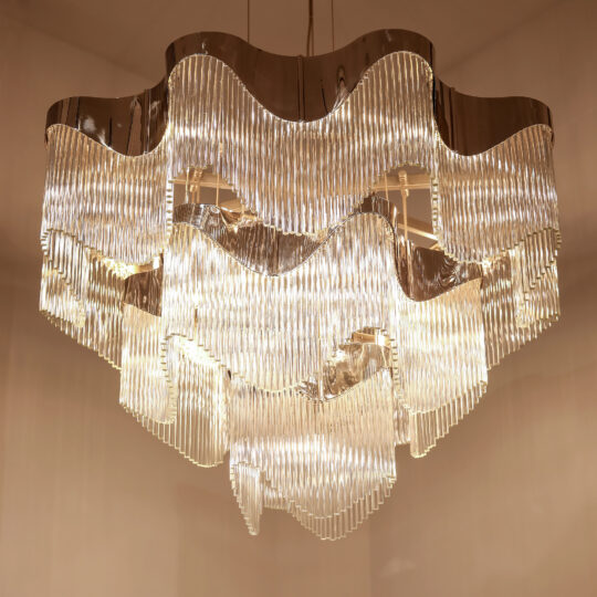 The Contemporary Wavy Tiered Chandelier has multiple tiers of clear, vertically arranged glass rods that reflect and diffuse warm light, giving any neutral ceiling an elegant and luxurious look.
