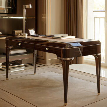 Exclusive Designer Writing Desk The Exclusive Designer Writing Desk, featuring drawers and metallic accents, stands in a bright room. Its sleek wooden top holds books, a lamp, notepad, and framed photo, complemented by large windows and elegant neutral decor.