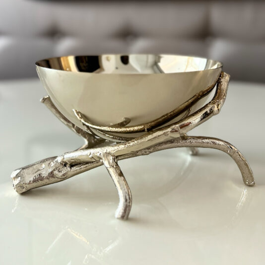 The Nut Bowl On Branch Design features a sculptural stand shaped like intertwined silver branches and is displayed on a glossy white surface with a softly blurred background.