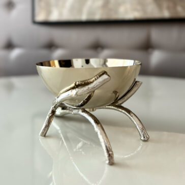 The Nut Bowl On Branch Design features a shiny silver bowl resting on a sculpted metal stand with three branch-like legs, displayed on a glossy white surface against a softly blurred background.