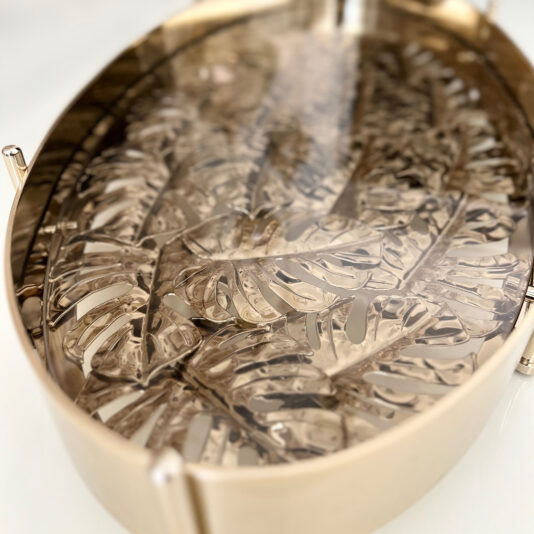 A close-up of the Tropical Leaf Oval Tray With Feet, showcasing an intricate raised monstera leaf pattern, reflective finish, smooth rounded edges, and sturdy feet for an elegant display.