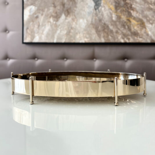 A Tropical Leaf Oval Tray With Feet stands on a glossy white surface by a tufted wall and abstract artwork, offering an elevated, stylish display.