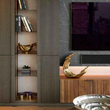 A modern living room features dark wood shelves, books, gold bowls, small blue jars, a large wall-mounted TV, and a black marble wall with white veining accented by the Luxury Decorative Wave Ornament.